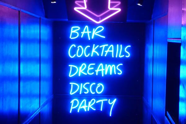 A bright purple neon arrow pointing to a cocktail bar entrance.