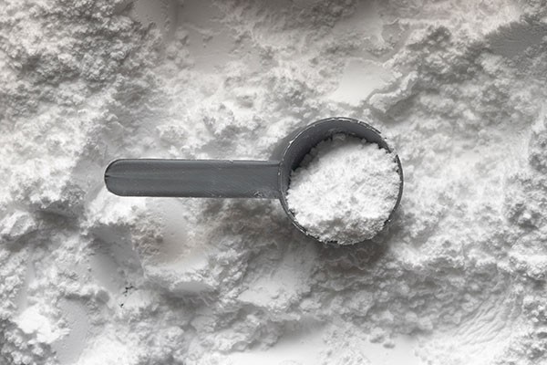 A scoop of pure creatine monohydrate powder resting on a bed of creatine, showcasing its role in strength, muscle growth, and workout recovery.