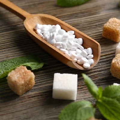 A wooden spoon holding white granulated artificial sweeteners.