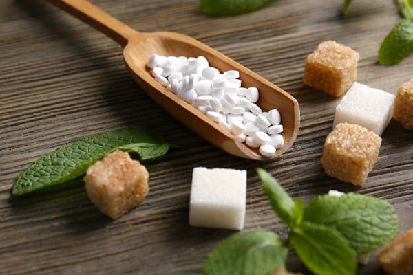 A wooden spoon holding white granulated artificial sweeteners.