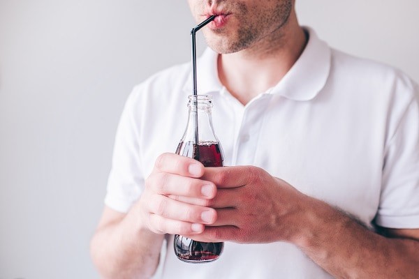 A man drinking a fizzy drink through a black, plastic straw.