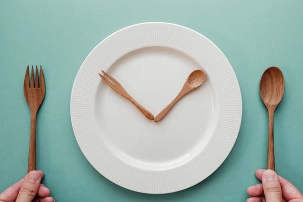 A small wooden fork and spoon on a white plate made to look like the hands on a clock.