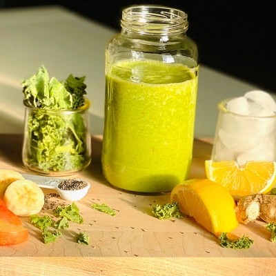 Apple, banana, ginger, orange, kale, and ice, all blended together to make a tasty looking green smoothie.
