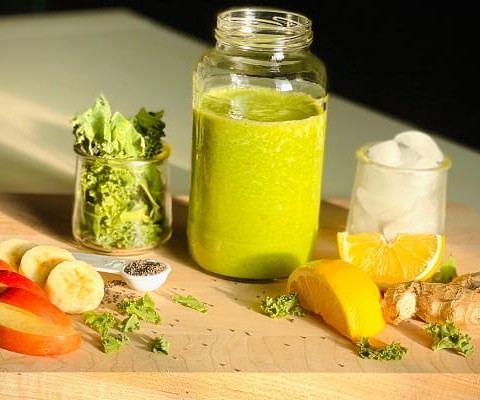 Apple, banana, ginger, orange, kale, and ice, all blended together to make a tasty looking green smoothie.