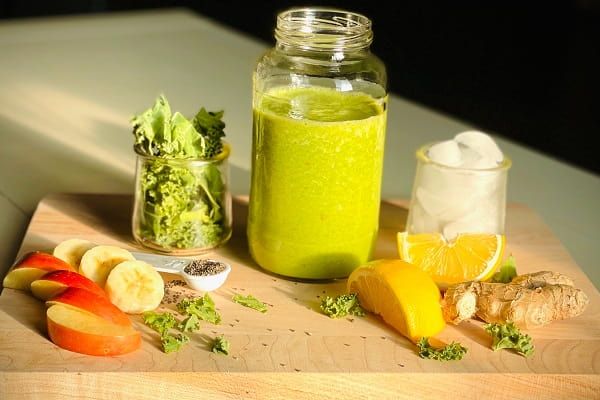 Apple, banana, ginger, orange, kale, and ice, all blended together to make a tasty looking green smoothie.