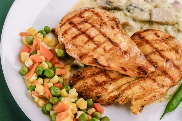 Two tasty seared chicken breasts and a side of peas, corn and carrots.