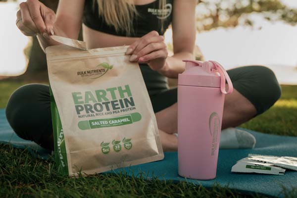 Bulk Ambassador Nicole Frain opening a bag of Bulk Nutrient's Earth Protein Salted Caramel and using her pink Stainless Steel Shaker.