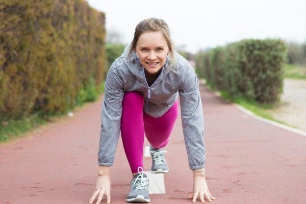 A smiling women in a low stance preparing to run. 
