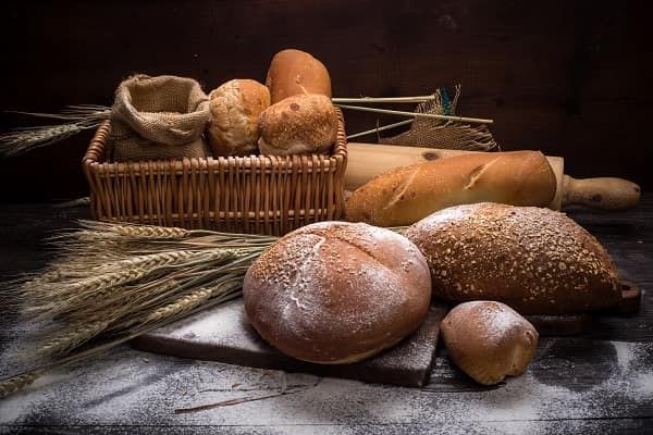 A bench top with varies kinds of breads and wheat.