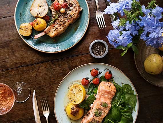 A delicious salmon fillet salad and a pork chop and veg meal at a fancy restaurant.
