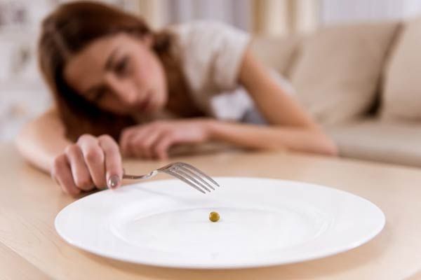 A hungry women using a fork to reach for a single pea on a plate.