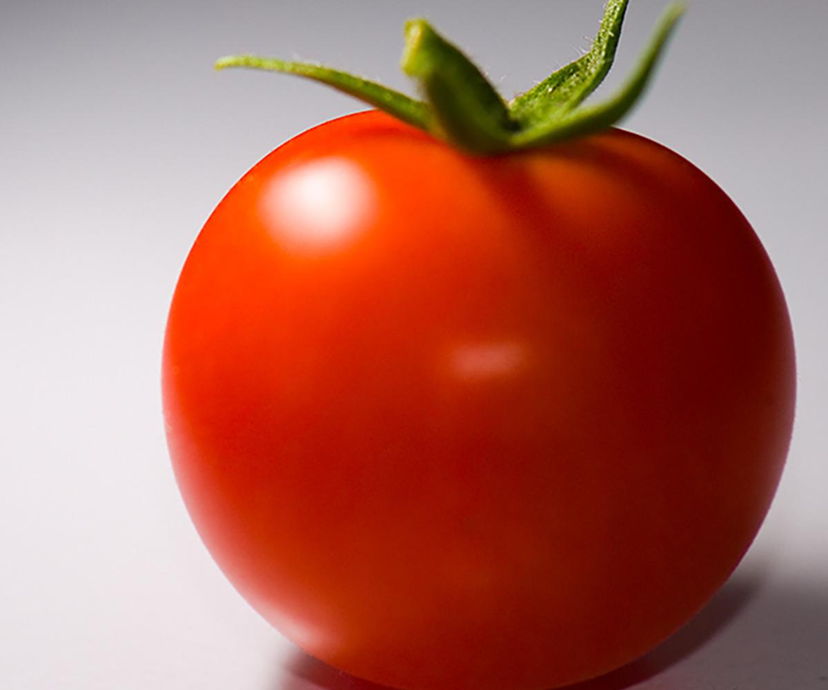 A women holding a clear, glass bowl that contains a variety of different fruits and vegetables with a body measuring tape draped on top.