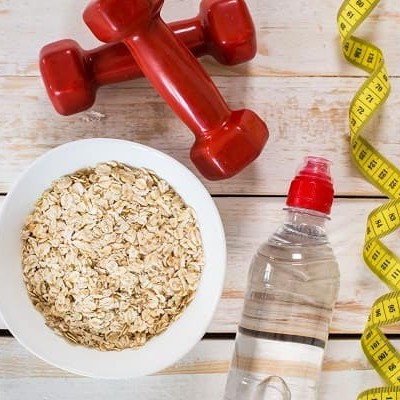A bowl of oatmeal, two dumbbells, a drink bottle, and a body tape measure.