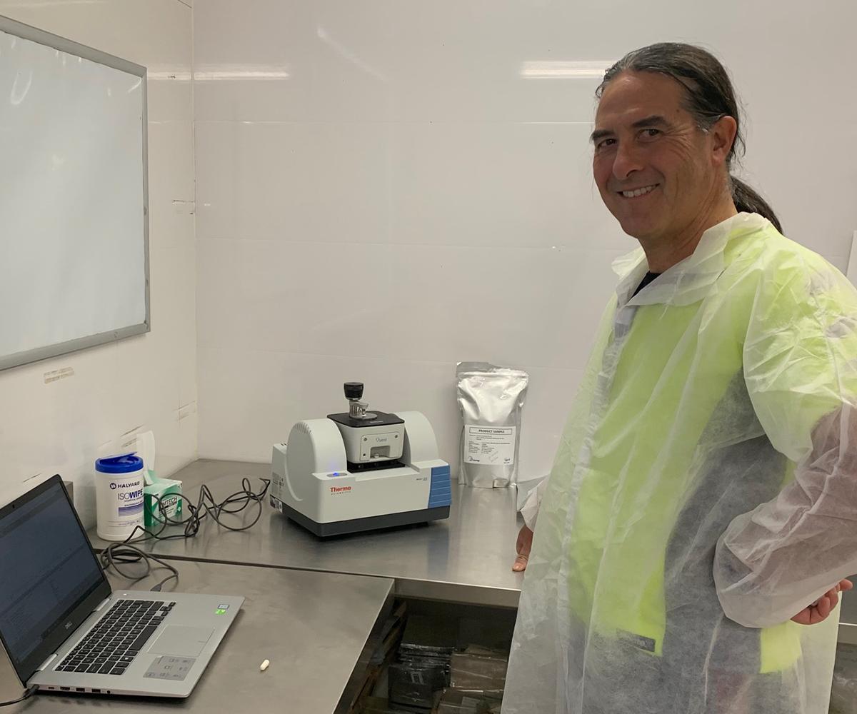 Lab technician in protective gear standing beside testing equipment in a food safety laboratory