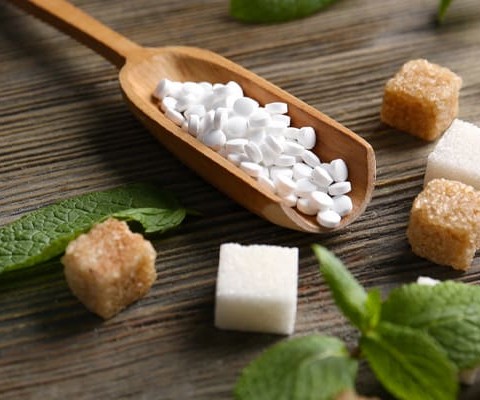 A wooden spoon holding white granulated artificial sweeteners.