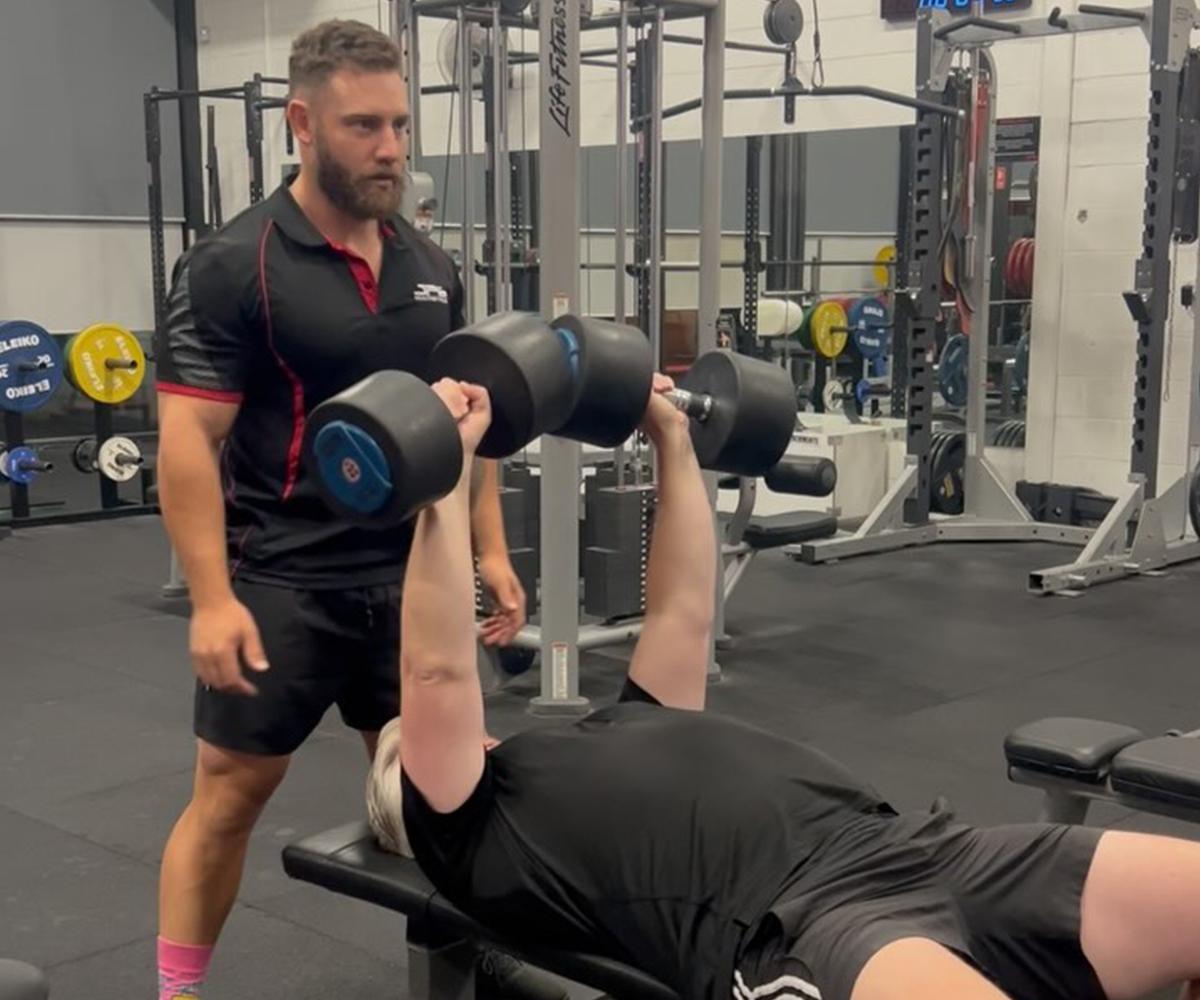 BN Ambassador Sam Schepis spotting for a client in the gym