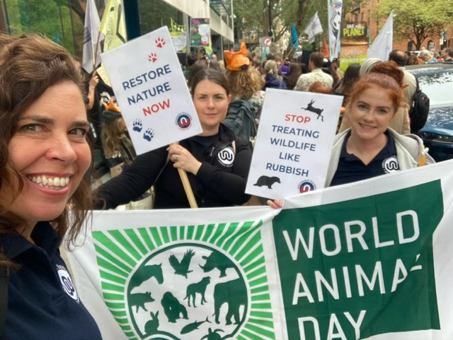 Three white women with signs for World Animal Day. Tash's sign says 'Stop treating wildlife like rubbish'