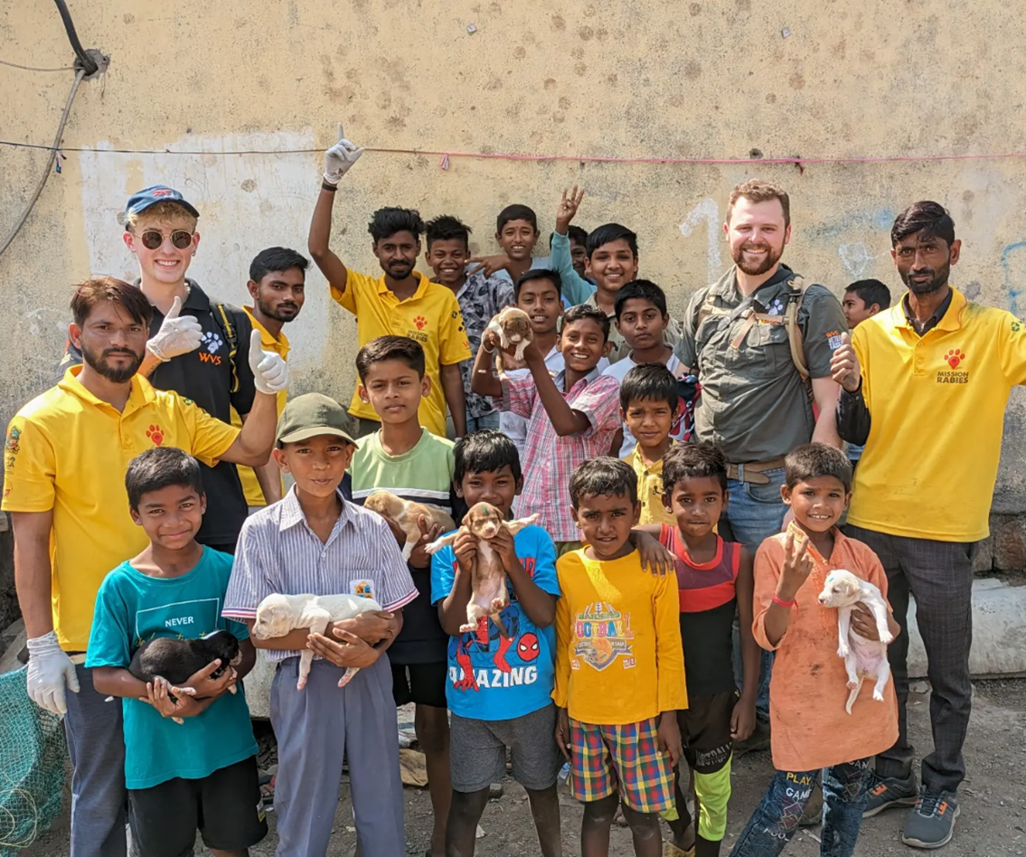 Dr Ben stands with a group of children and adults, some holding puppies who have been vaccinated, in Mumbai.