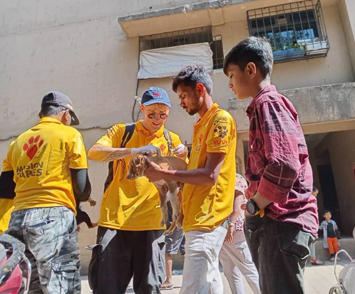 Dr Ben vaccinates a brown puppy against rabies, helped by two Mission Rabies team members and a child.