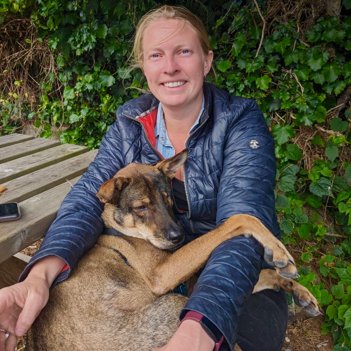 The same dog as an adult, laying comfortably on the lap of a smiling white woman with blonde hair