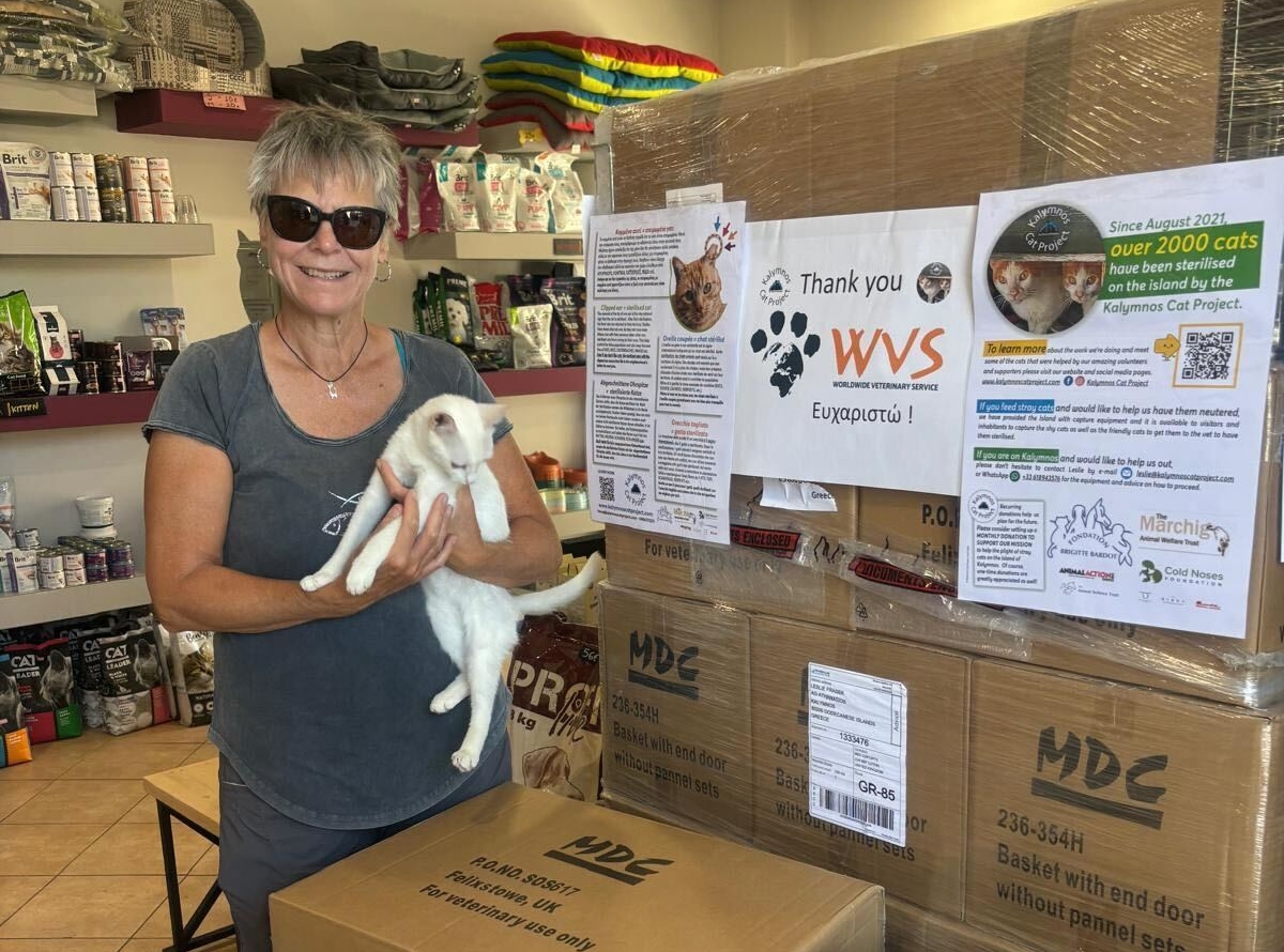 A woman holds a white cat, standing next to a delivery of supplies donated from WVS