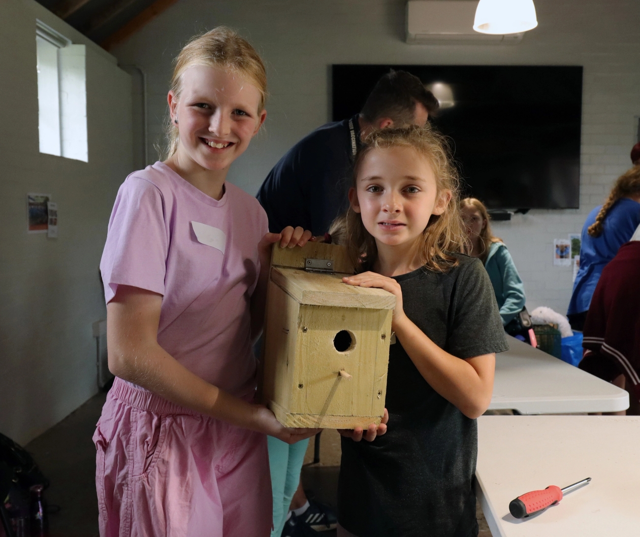Two children hold a bird box they've built