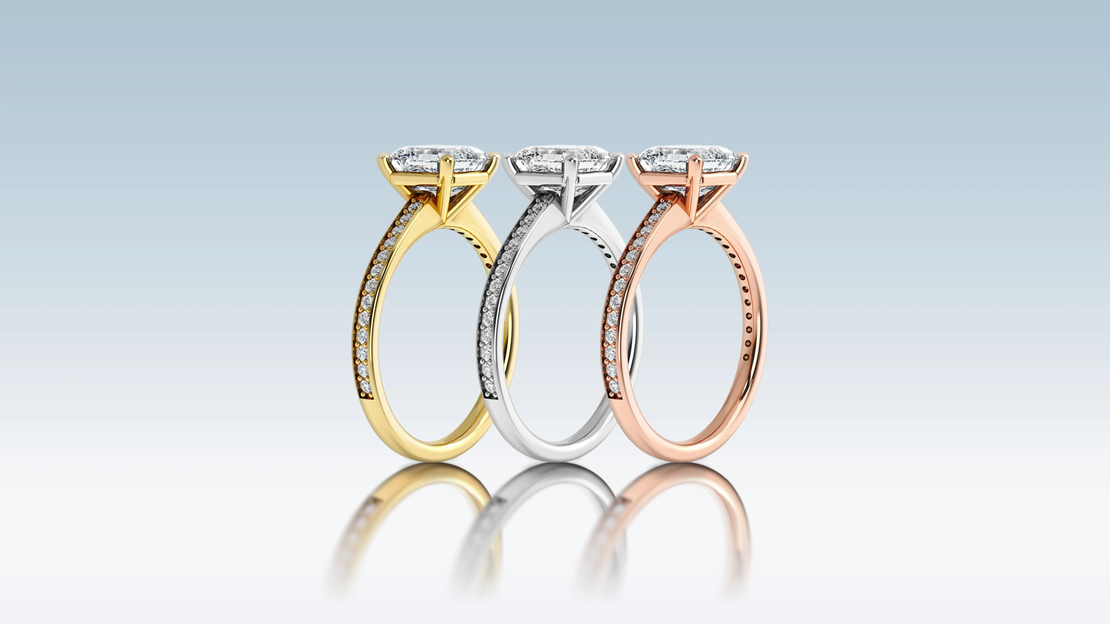 Three solitaire rings in yellow gold, white gold, and rose gold, each set with a rectangular diamond