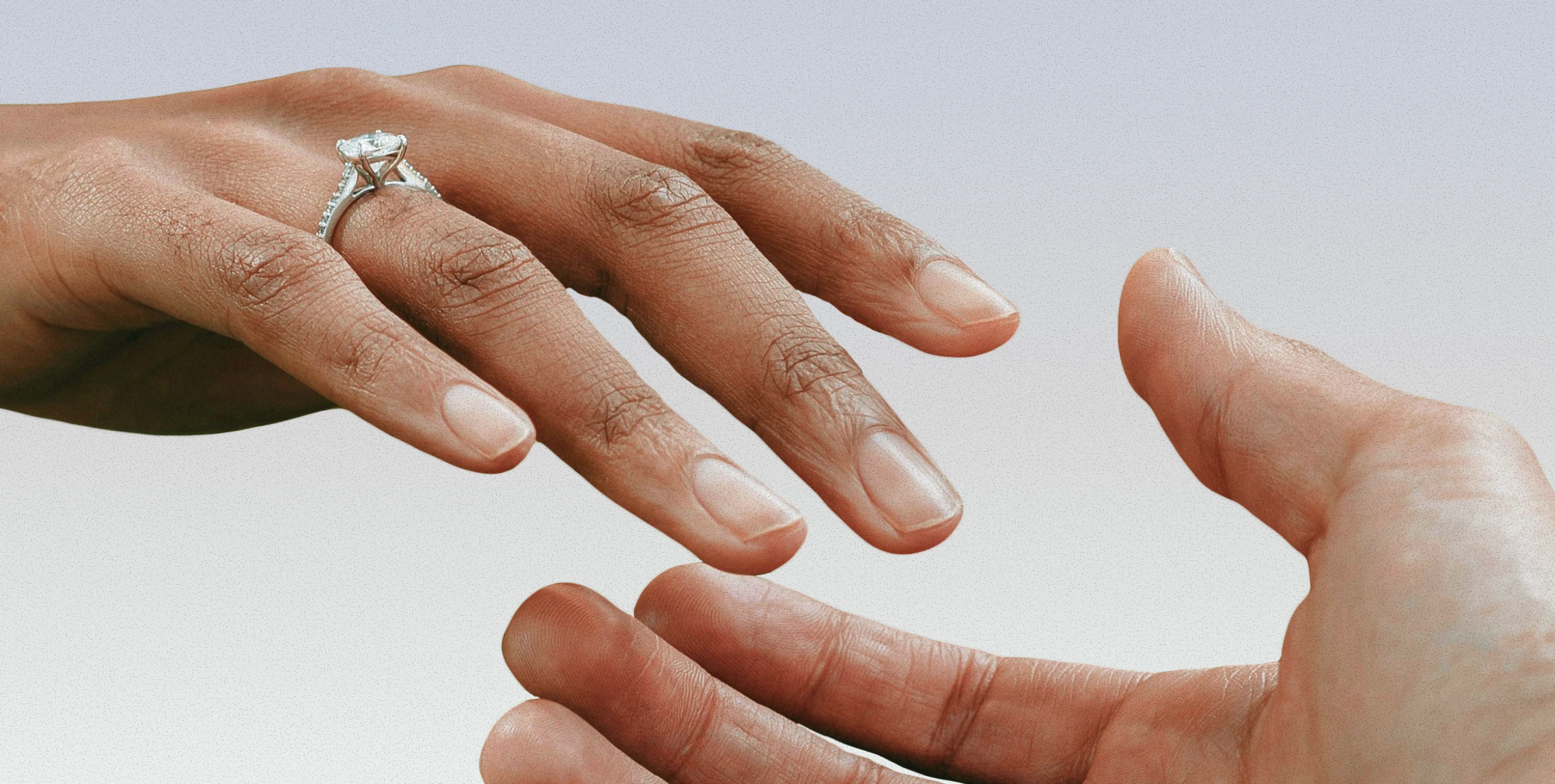 Hand wearing a diamond engagement ring reaching toward another hand