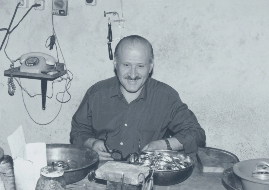 Jeweler at the workbench with rings and tools, holding his glasses