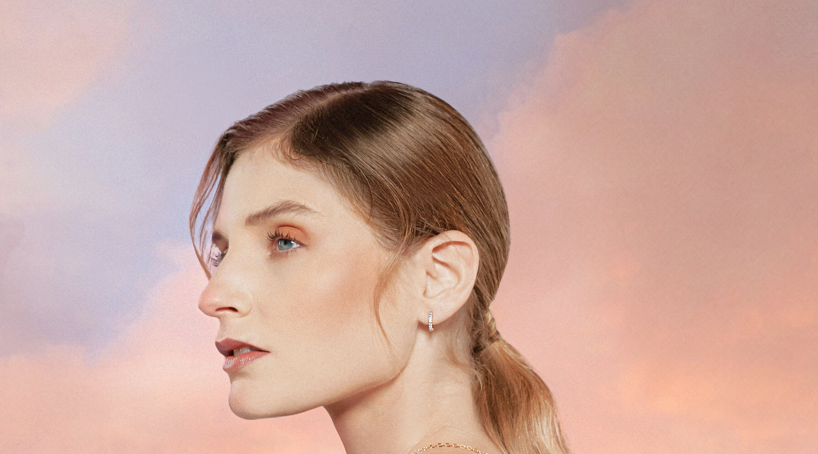 Woman in profile wearing a diamond hoop earring against a sunset sky