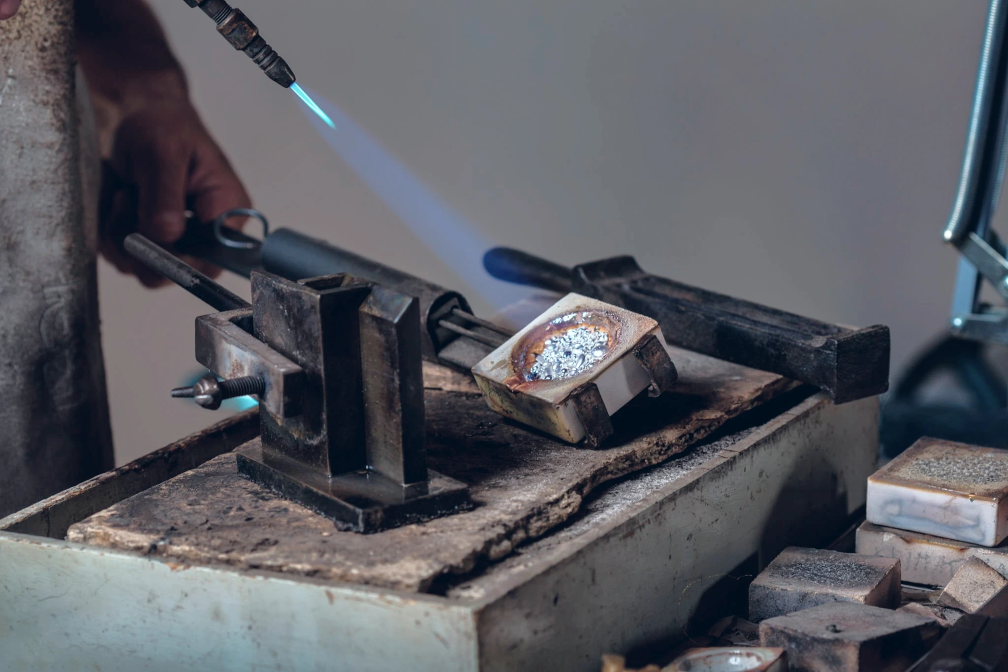 Jeweler heating precious metal with a torch at a workshop bench
