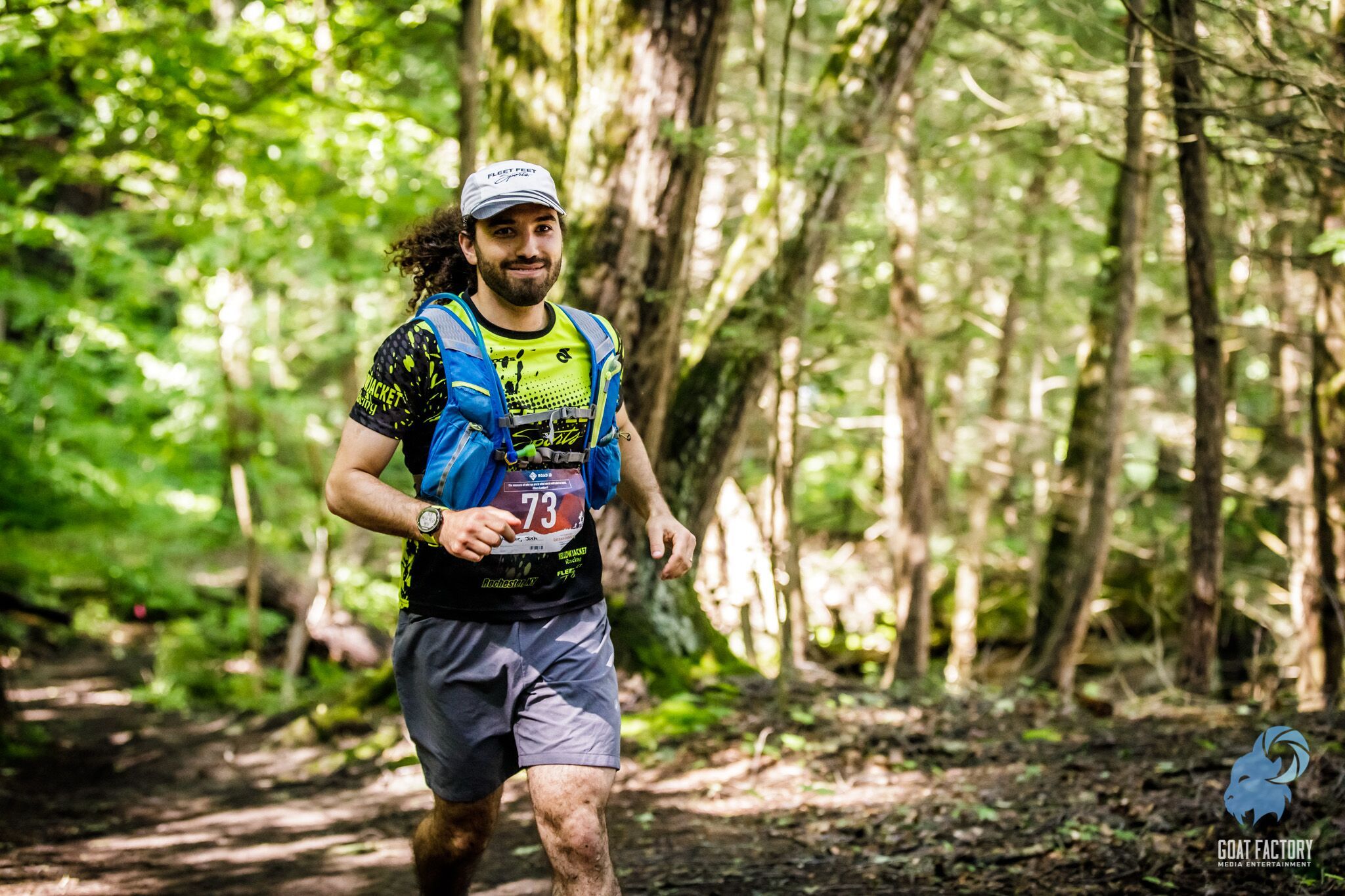 Photo of me taken by Goat Face Media in the woods at mile 22, smiling trying to hide the fact there is food in my mouth