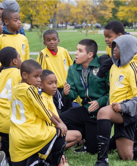 Entrenador hablándole a un equipo de niños que juegan al fútbol.