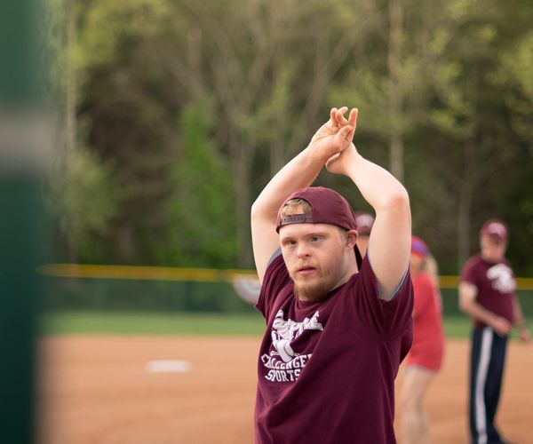 A child wearing a Burgandy baseball outfit with his hands raised above his head 