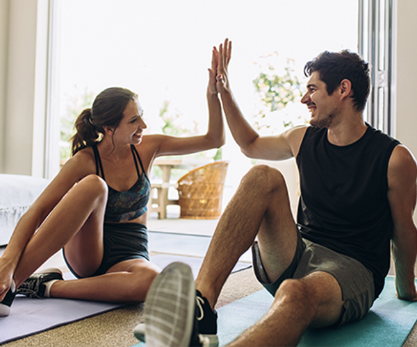 man and woman sitting on yoga mats high fiving