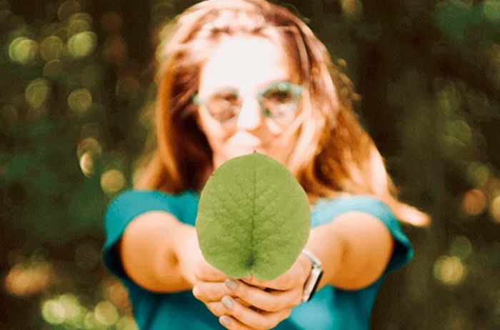 mulher com óculos de sol verdes segurando uma folha verde para a câmera