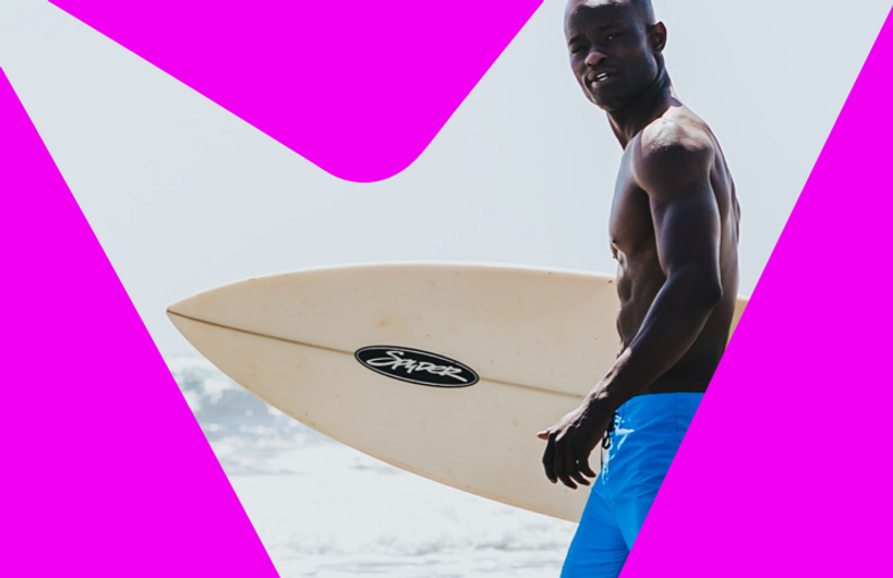 Un homme au short bleu vif transportant une planche de surf sur la plage 