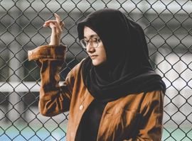 A girl in a brown jacket looking nervous by a chain link fence