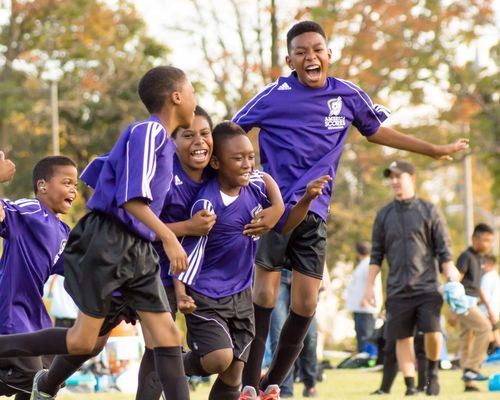 Four young kids in purple football kits celebrating a goal