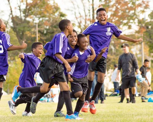 Quatre jeunes enfants qui portent un uniforme de soccer violet célébrant après avoir marque un but