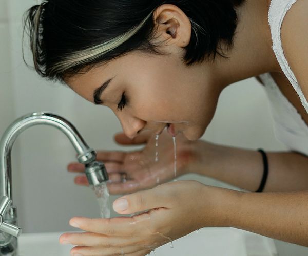 Une fille est penchée sur un lavabo et se lave le visage alors que le robinet coule  