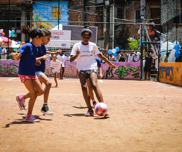 Young girls playing soccer on a sandy soccer pitch