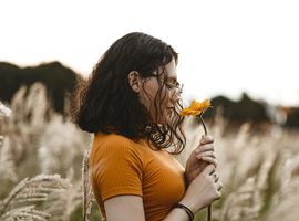Une femme sentant une fleur de couleur orangée dans un champ 