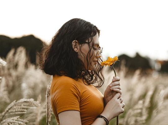 Une femme sentant une fleur de couleur orangée dans un champ 