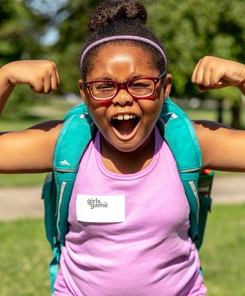 A young girl from Girls Game jokes as she flexes her biceps in the park