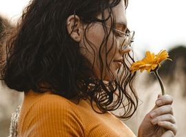 Una niña con pullover amarillo está parada en la naturaleza mientras huele una flor amarilla