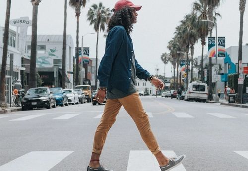 Hombre con una gorra roja y camisa de manga larga y pantalones, cruzando la calle.