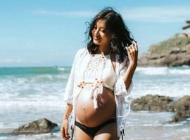 Femme enceinte riant sur la plage en bikini.