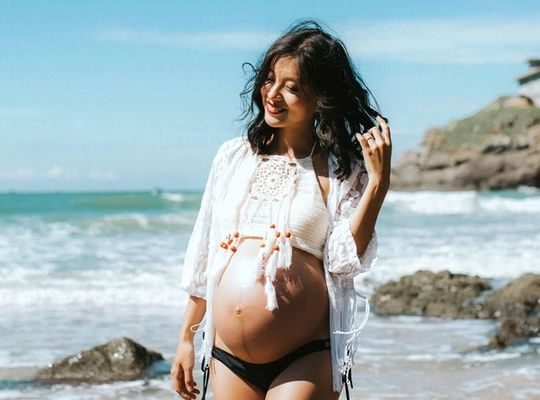 Femme enceinte riant sur la plage en bikini.