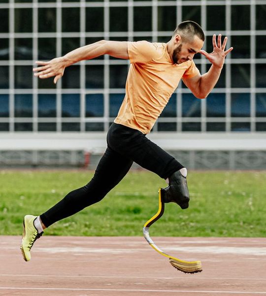 Mann mit einem oragenen T-shirt, einer schwarzen Leggins und einer rechten Beinprothese rennt.